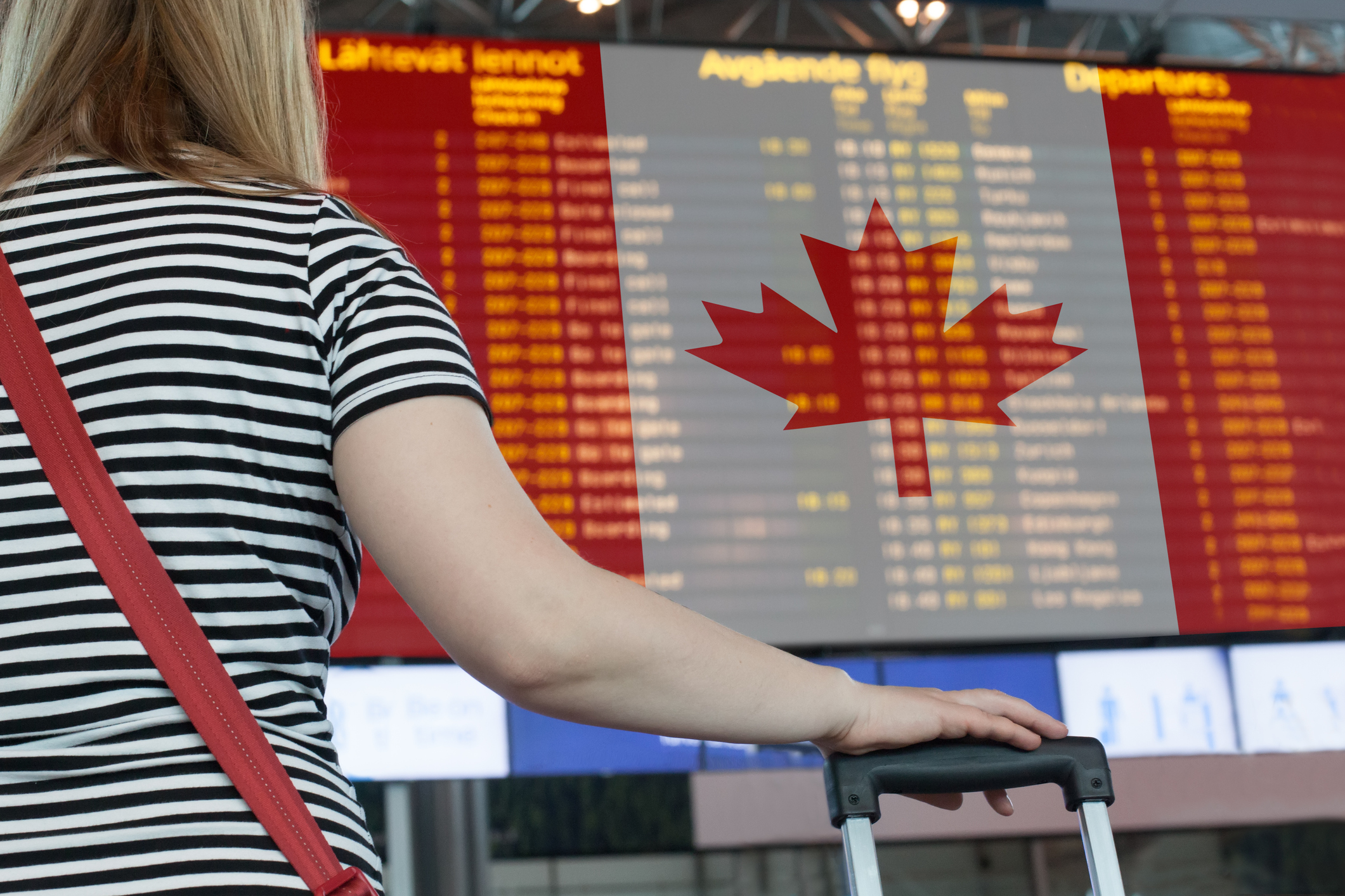 Person with luggage in front of Canadian flag